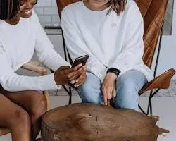 Two girls gathered around a smartphone, their faces lit by the screen, participating in a social media girls forum.