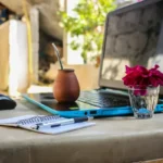 Laptop with a glass of water, another drink, and a pen on a desk, featured in the article 'The Many Struggles of a Digital Nomad and How to Deal with Them.