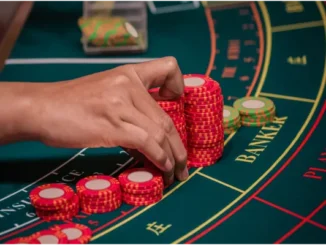 Hand placing red and white casino chips on the "Banker" section of a baccarat table.