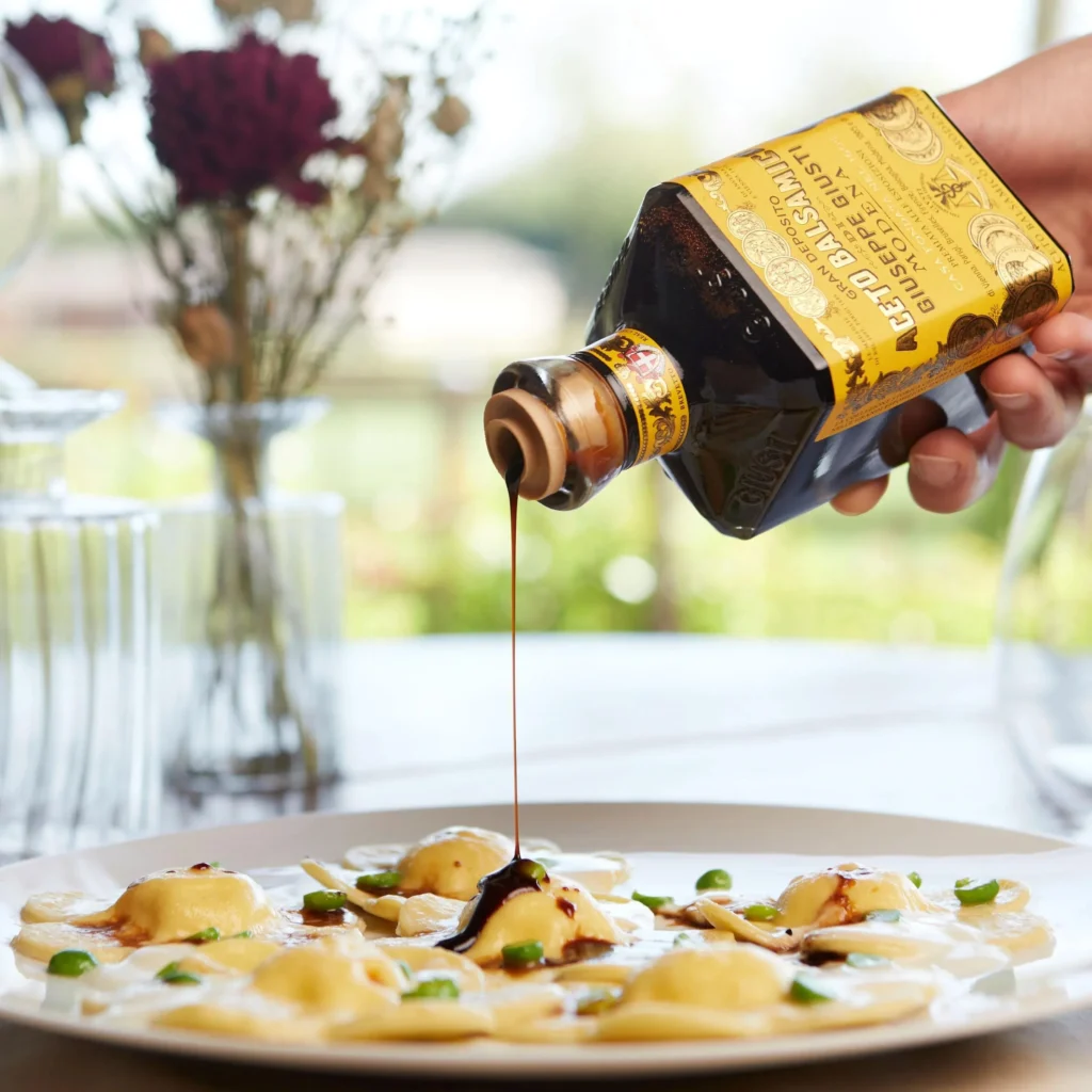 Bottle of Giuseppe Giusti 4 Gold Medals Balsamic Vinegar being poured over ravioli.