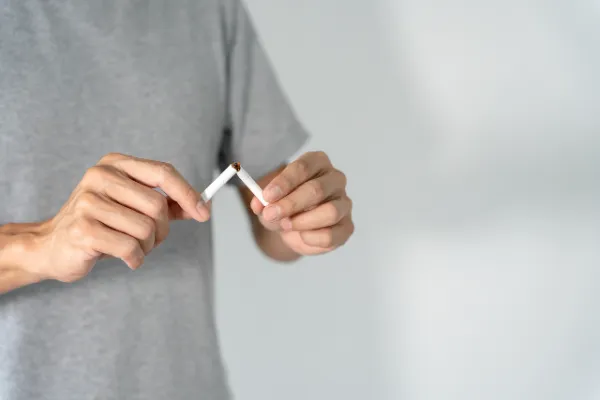 Person breaking a cigarette in half, symbolizing an action towards quitting and overcoming addiction.