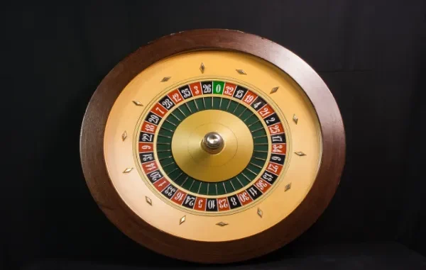 A close-up, top-down view of a classic wooden roulette wheel with red, black, and green numbered slots, centered against a dark background.