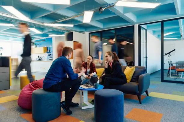 Blurred figures moving through a dynamic office space where a small group is meeting in a relaxed setting.