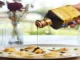 Hand pouring dark, viscous balsamic vinegar from a labeled bottle onto a plate of ravioli.