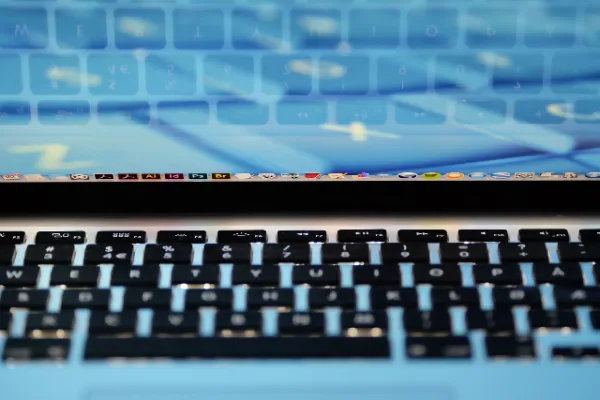 Close-up of a MacBook Pro keyboard with a screen reflecting app icons, suggesting software use for business.