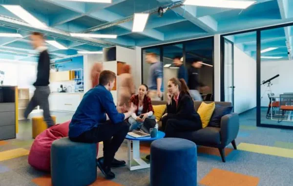People collaborating in a modern, activity-based office setting, discussing ideas in a comfortable lounge area.