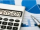 A calculator showing the word "PENSION" on its display, placed on top of financial documents with charts and numbers, alongside a pen.