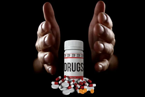 Hands reaching out to push away a bottle labeled "DRUGS" surrounded by pills, symbolizing the act of stopping drug use.