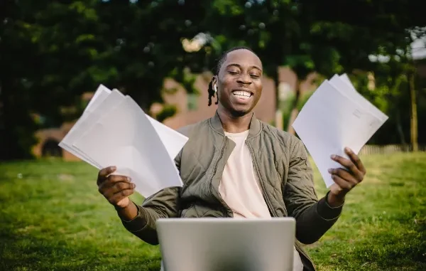 The Best Essay Writing Strategy: Unlock Your Path to Success Smiling person outdoors with laptop and papers, celebrating success.
