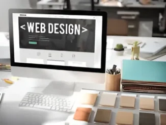 A computer monitor displaying "WEB DESIGN" with an opening and closing tag, on a desk with design tools and color swatches.
