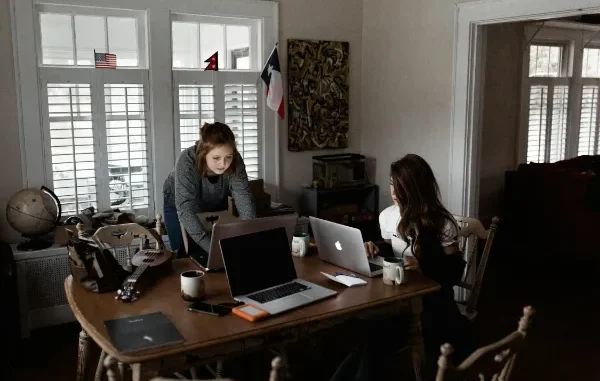 Two women working on laptops on a wooden table, on their small business.