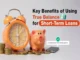 A bright orange alarm clock stands beside a peach-colored piggy bank, both surrounded by scattered stacks of gold coins. A black smartphone to the right displays a pop-up message: "Congratulations! Your loan has been approved." The text "Key Benefits of Using True Balance for Short-Term Loans" is prominently displayed in black, blue, and orange on the right side of the image.