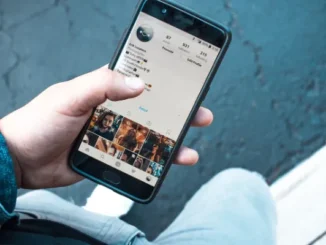 Person holding a smartphone displaying an Instagram profile with photo posts.