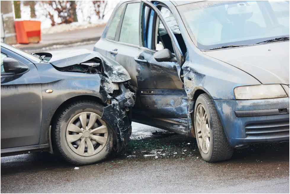 Wrecked cars, one dark, one light blue, after a traffic collision at a city intersection.