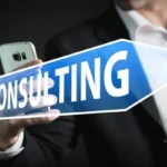 A person in a suit holding a smartphone and a blue arrow sign with the word "CONSULTING," symbolizing expert guidance for business solutions.
