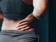 A hand gently holding a person's lower back, indicating potential pain or discomfort.
