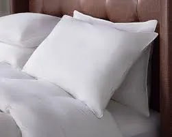 A close-up shot of several plump, white pillows with crisp white pillowcases on a bed, suggesting luxury hotel bedding, with a brown upholstered headboard in the background.