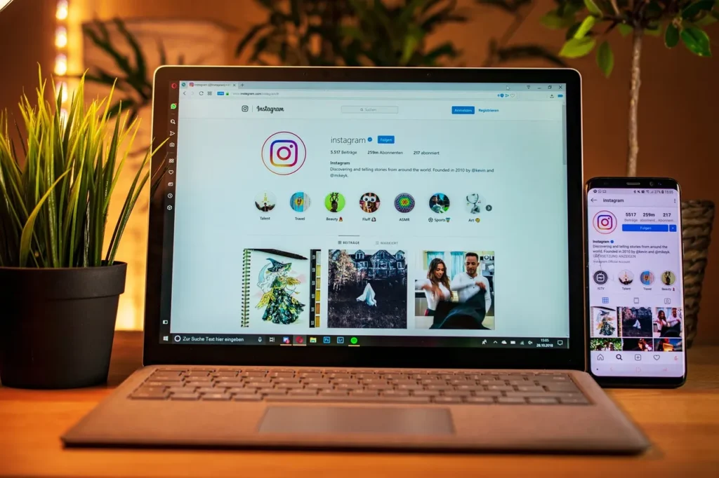 Laptop and smartphone displaying an Instagram profile on a wooden desk with indoor plants.