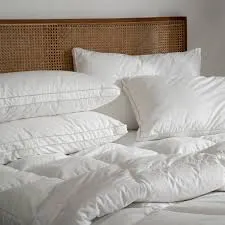 A bed with a woven rattan headboard featuring multiple plump white pillows with grey piping and a white duvet, suggesting luxurious and comfortable bedding.