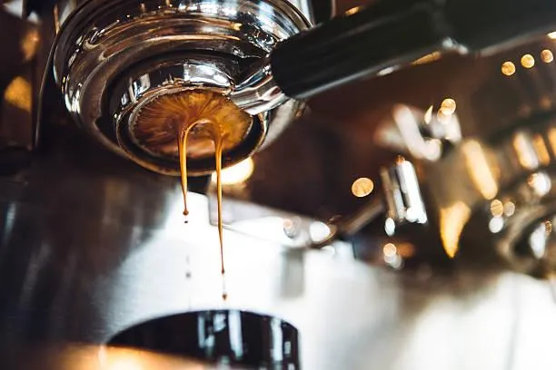 A stream of rich espresso flowing from the spouts of a metal portafilter into a white cup.