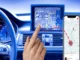 A hand touching a car's dashboard display showing a navigation map, with a smartphone displaying a taxi dispatch app and route overlay to the right.