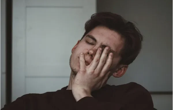 Symptoms and Support for Wellbutrin Withdrawal A young man with his eyes closed, rubbing his face with his hand, looking tired or overwhelmed.