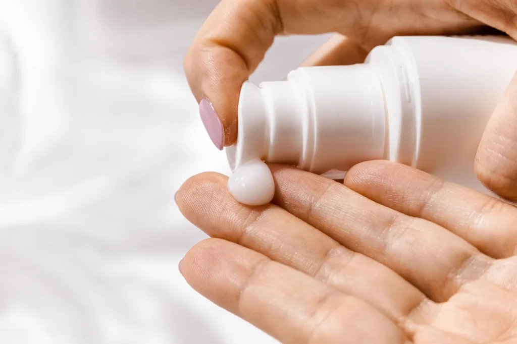 A hand gently dispenses a pearl-sized drop of white, creamy product from a pump bottle onto the palm, symbolizing the application of a beneficial skincare product for oily or acne-prone skin.