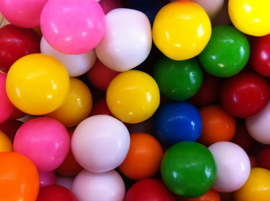 A close-up, top-down view of a vibrant pile of assorted colorful gumballs in shades of pink, yellow, green, blue, white, orange, and red.