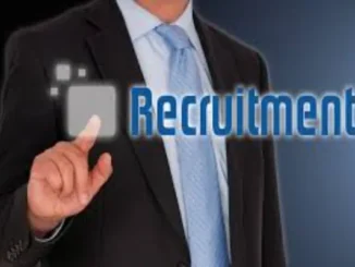 A man in a suit and tie points to a glowing, transparent screen displaying the word "Recruitment," symbolizing digital hiring processes.