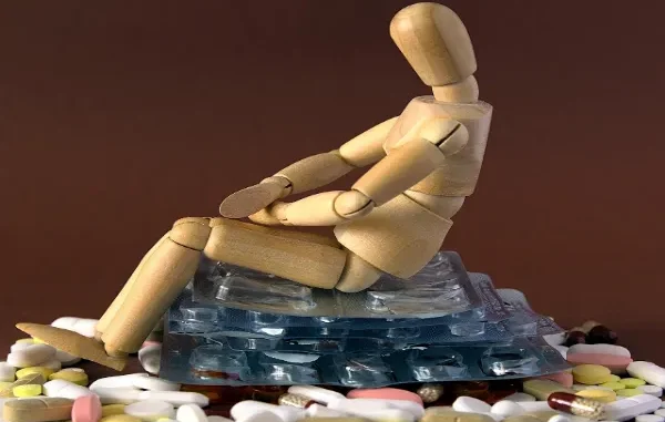 The Burden of Addiction A wooden mannequin figure sits slumped on a pile of various pills and blister packs, symbolizing drug addiction and its burden.