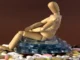 A wooden mannequin figure sits slumped on a pile of various pills and blister packs, symbolizing drug addiction and its burden.