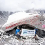 Two people pose with a 'Nepal High Trek Everest Base Camp (5364m)' banner in front of a large, rock marked with red paint at Everest Base Camp.