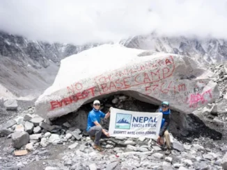 Two people pose with a 'Nepal High Trek Everest Base Camp (5364m)' banner in front of a large, rock marked with red paint at Everest Base Camp.