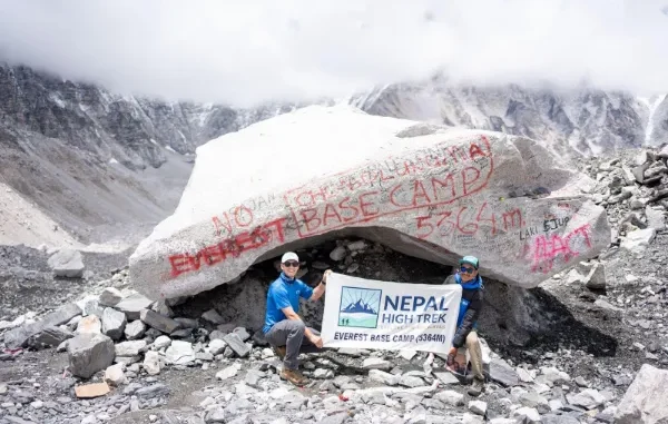 Everest Base Camp Achievement Two people pose with a 'Nepal High Trek Everest Base Camp (5364m)' banner in front of a large, rock marked with red paint at Everest Base Camp.