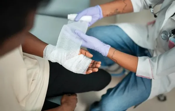 A medical professional or first responder is shown bandaging the hand of an injured person, illustrating the need for prompt medical care following an accident.