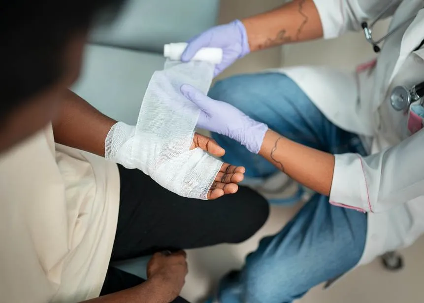 A medical professional in purple gloves carefully wraps a white bandage around the hand of an injured person, suggesting immediate medical attention after an accident.