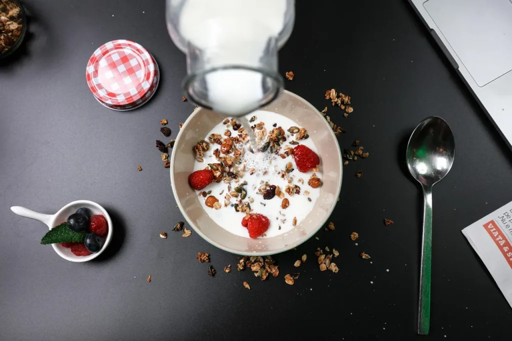 A bowl of healthy breakfast cereal topped with sliced bananas, sitting on a red and white checkered tablecloth, with a glass of orange juice in the background, representing a balanced start to the day for hair health.