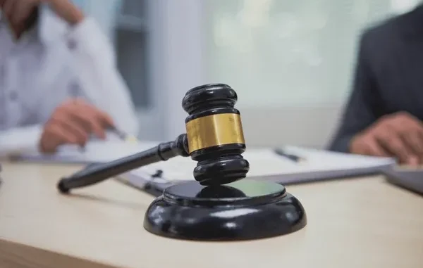 kentucky personal injury gavel A wooden gavel rests on a desk in the foreground, with blurred figures of people in professional attire discussing documents in the background, symbolizing legal proceedings or a court of law.