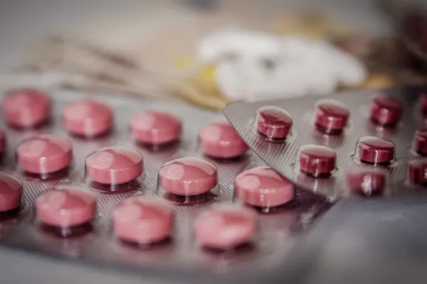 A close-up of two blister packs of pink pills, with one pack partially opened, against a blurred background.