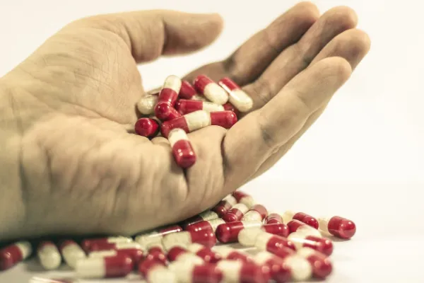 A hand holding a pile of red and white capsules, with more capsules scattered on a white surface below.