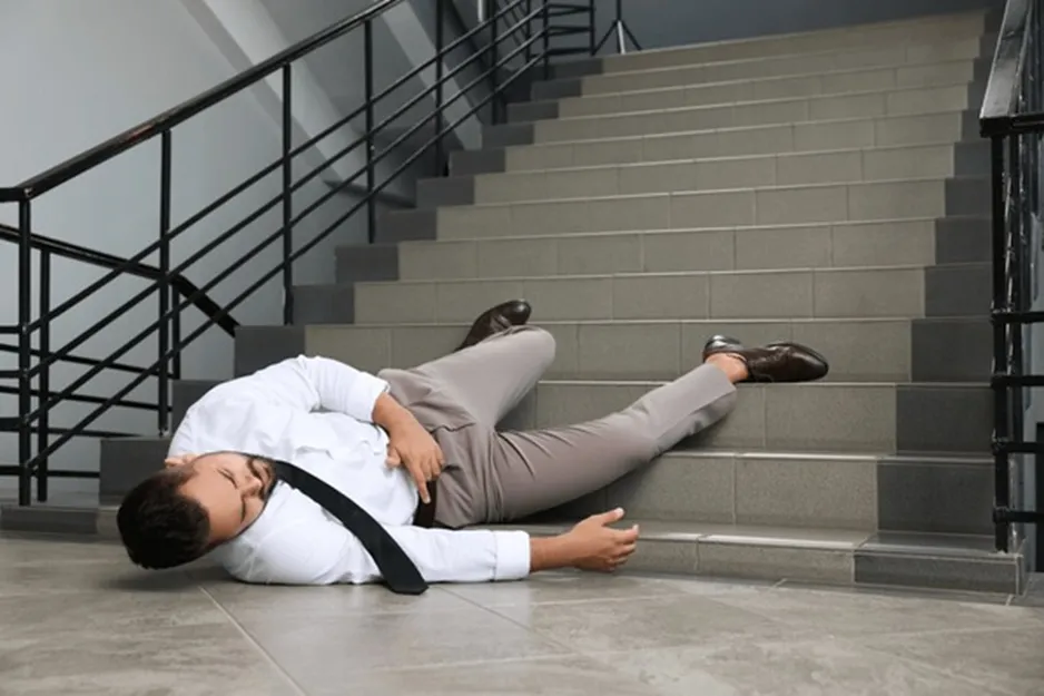 A man lies injured on a staircase, indicating a slip and fall accident, relevant to personal injury claims.