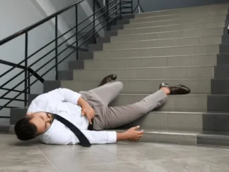 A man in a white shirt and khaki pants lying injured on the steps of a concrete staircase after a fall.