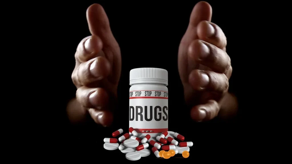 A bottle labeled "DRUGS" with scattered pills in front of it, and two hands raised in a stopping gesture in the background, symbolizing an intervention or decision to quit drugs.