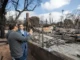 An insurance adjuster pointing out damage to a homeowner in the charred remains of a house after a wildfire.