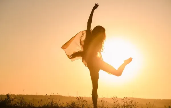 Silhouette of a happy woman dancing in the sunset, symbolizing freedom and body confidence after weight loss.