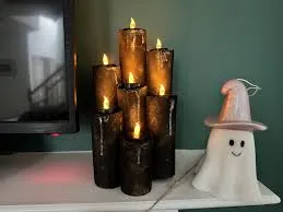 A group of tall, black, dripping-wax style LED candles are displayed next to a small white ceramic ghost figurine wearing a witch's hat, creating a spooky and festive Halloween mantel decoration.