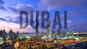 The word "DUBAI" is superimposed in large, semi-transparent letters over a nighttime panoramic view of the illuminated Dubai skyline featuring numerous skyscrapers.