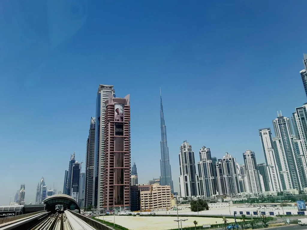 The iconic skyline of Dubai with the Burj Khalifa towering over modern residential and commercial buildings, viewed from a metro train track.