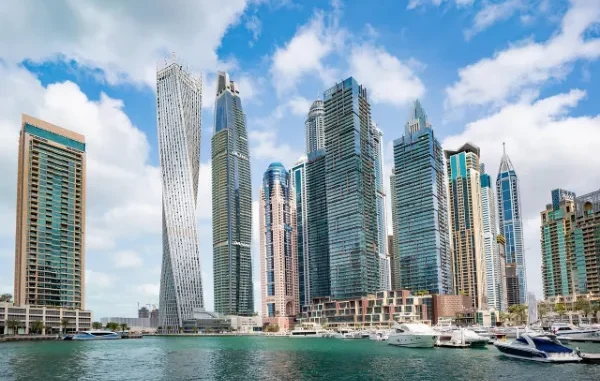 Dubai Marina: A Glimpse into the Luxury Lifestyle The modern Dubai Marina skyline featuring luxury skyscrapers and yachts docked in the harbor under a bright blue sky with scattered clouds.