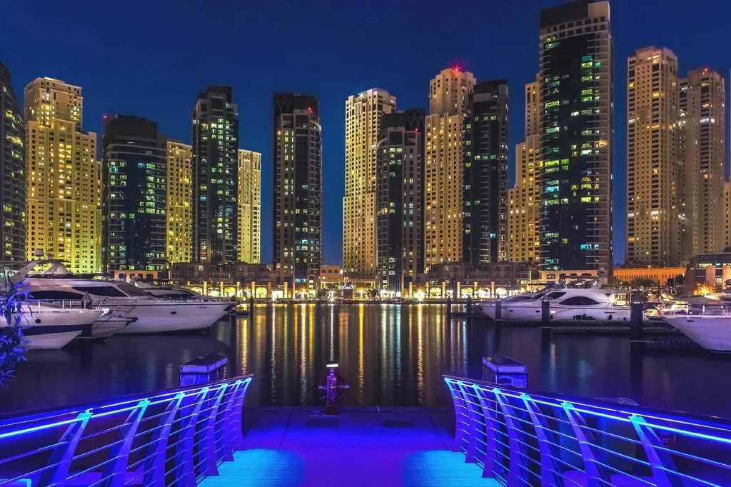 Dubai Marina at night with illuminated skyscrapers reflecting on the water and luxury yachts docked below.
